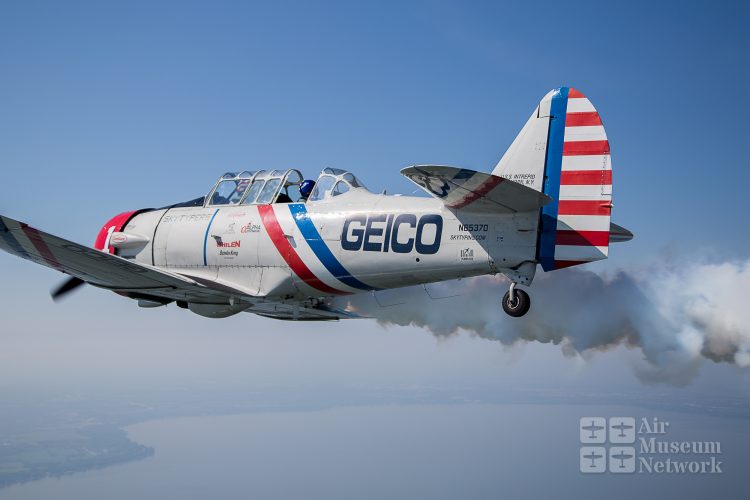 Geico Skytyper with smoke on over Oshkosh at EAA's AirVenture 2018 - photo by David Eckert -Air Museum Network